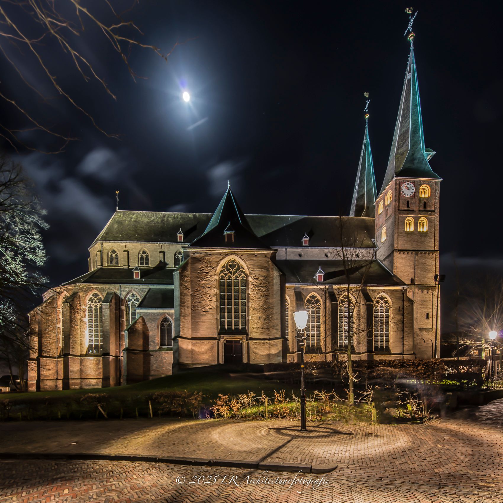 Een gotische kerk in Deventer bij avond, warm uitgelicht metselwerk en torenspitsen tegen een diepblauwe nachthemel met maanlicht.