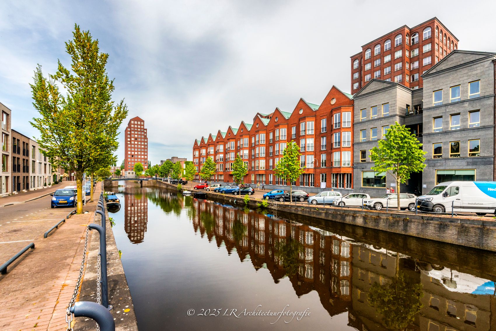 Een blok moderne baksteenarchitectuur langs het water, onder een blauwe lucht.