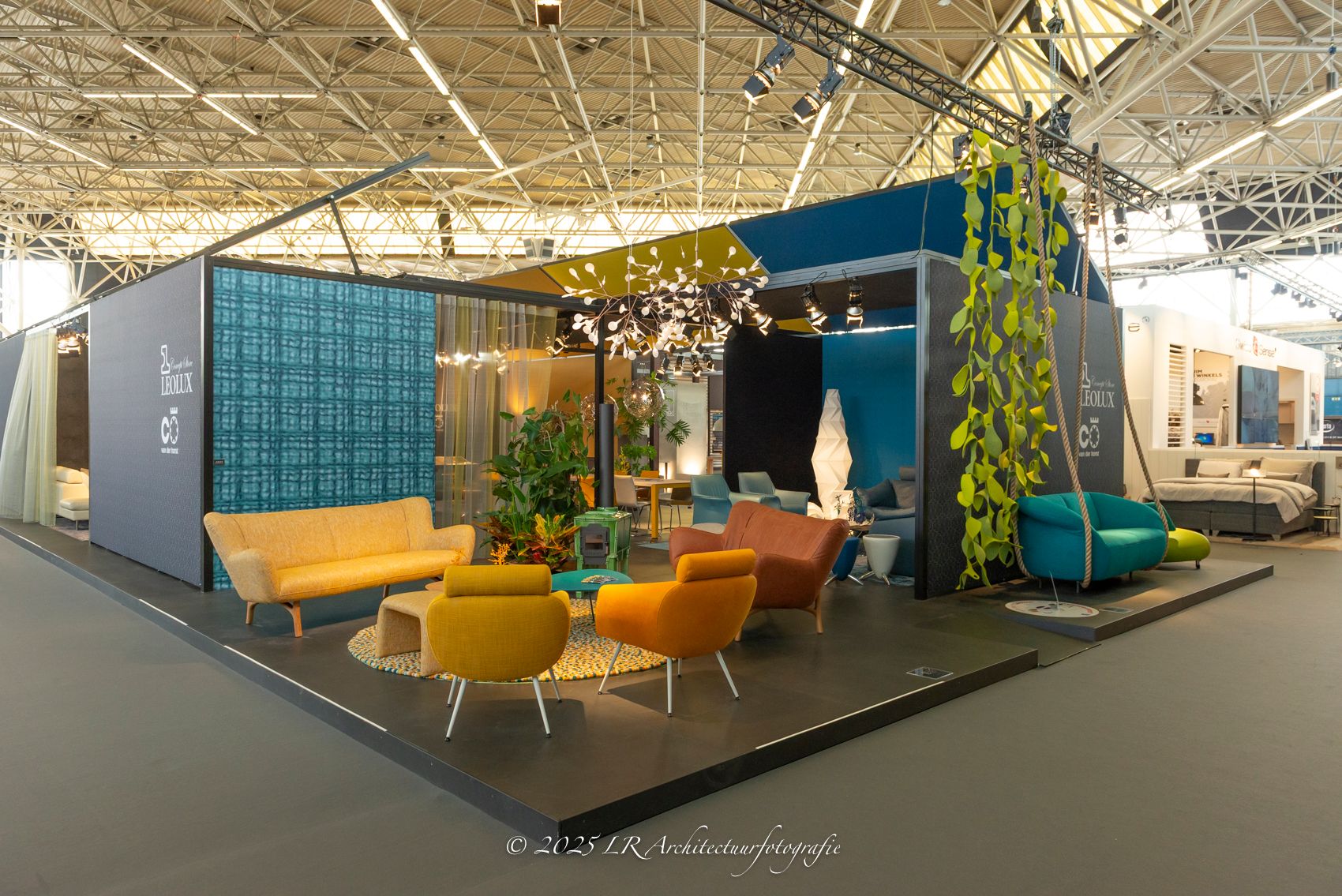 Een ingerichte woonvignette op een beurs, met warme kleuren, planten en design-meubilair rond een lage tafel.