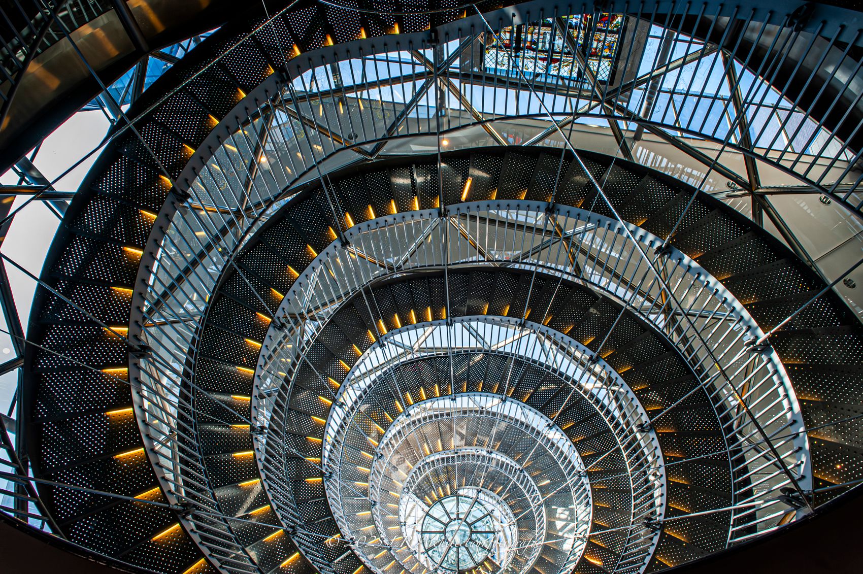 Een monumentale wenteltrap van bovenaf gefotografeerd, met een spiraalvormig, geometrisch patroon van treden en balustrades.