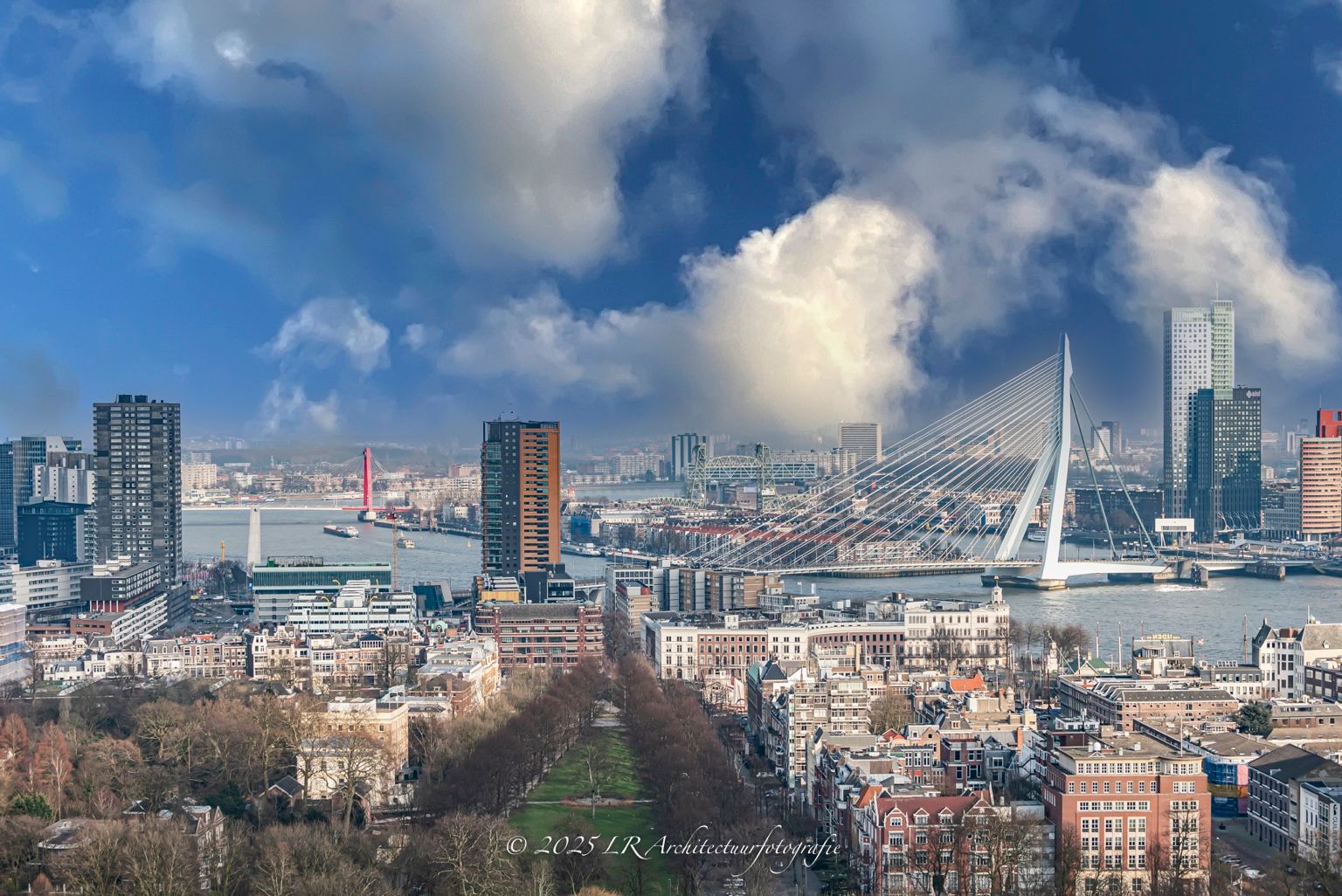 De skyline van Rotterdam met de Erasmusbrug onder een dramatische wolkenlucht, gezien vanaf hoogte.