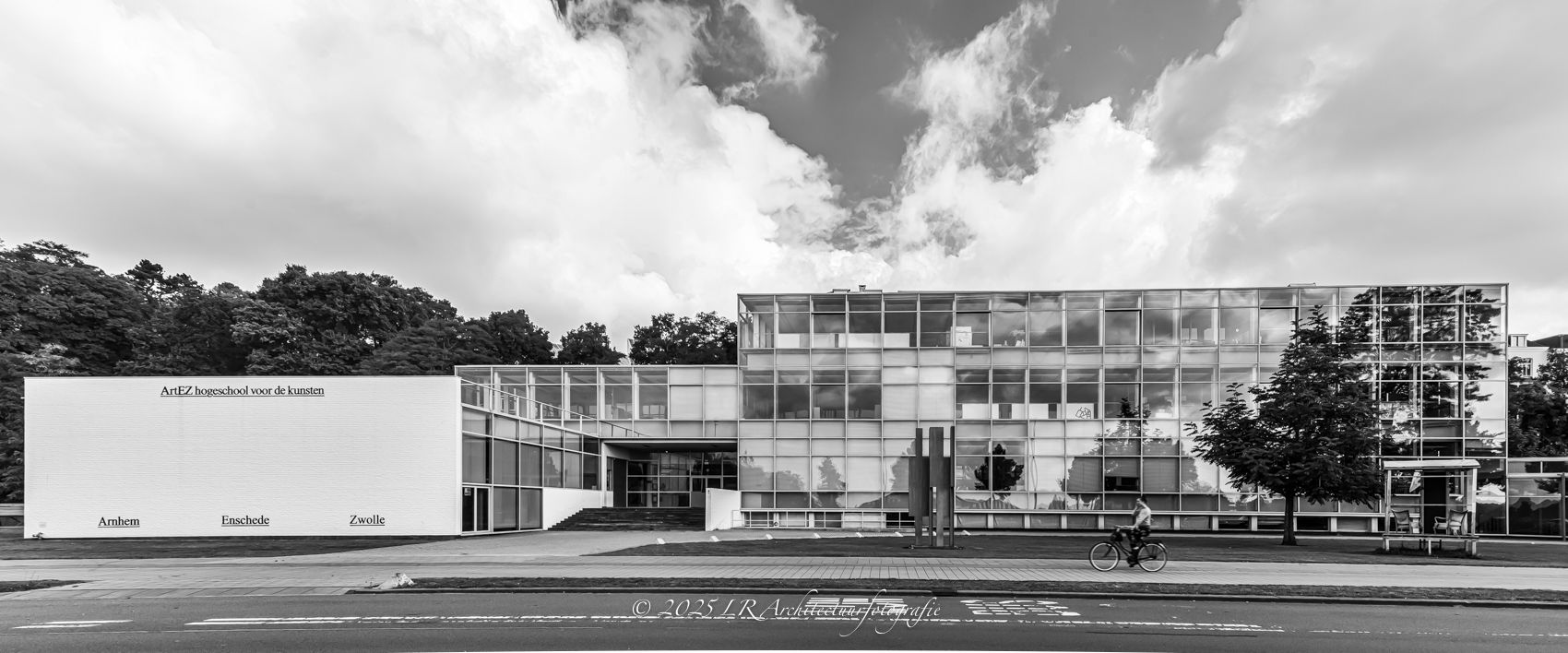 Gevel van de ArtEZ Hogeschool voor de Kunsten in Arnhem onder een dreigende wolkenlucht, met een fietser op de voorgrond.