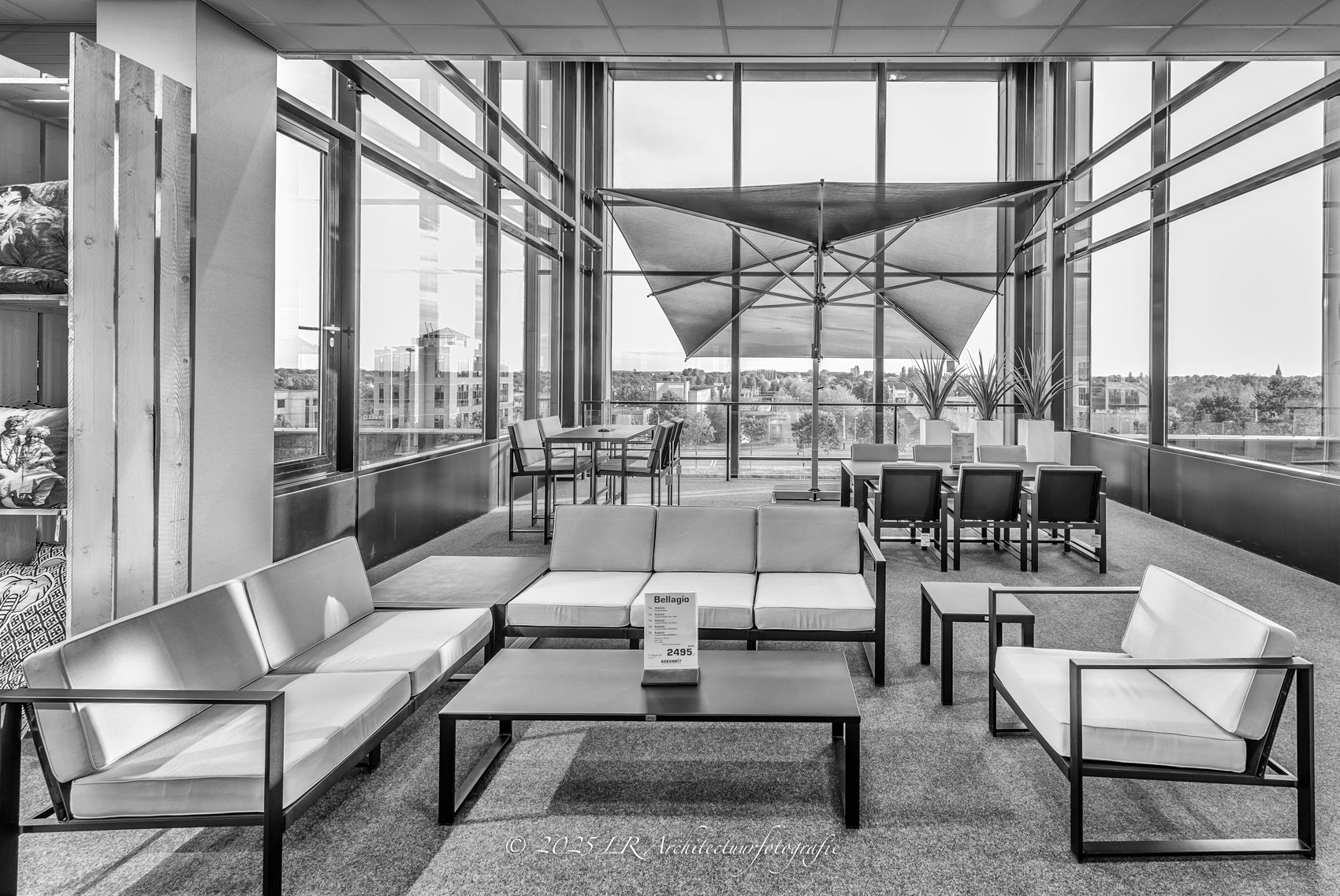 Een zithoek in zwart-wit met moderne banken en fauteuils langs een hoge glazen gevel.