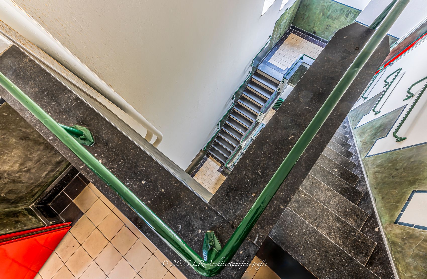 Een hedendaags interieur van bovenaf, met een groene structuurkolom, een donkere natuurstenen trap en kleurrijke accenten.