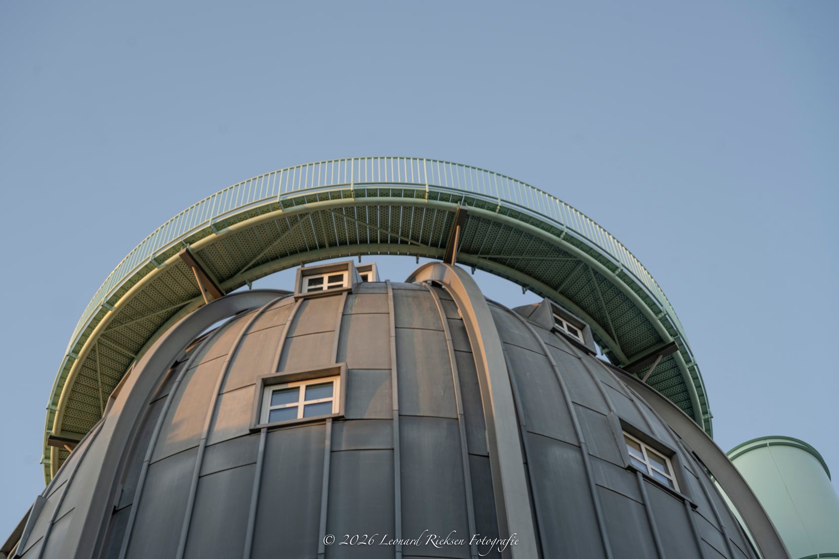 Dezelfde koepel recht van onderaf gefotografeerd, waarbij de verticale zinken banen en de gebogen loopbrug met balustrade een cirkel tegen de heldere lucht vormen.