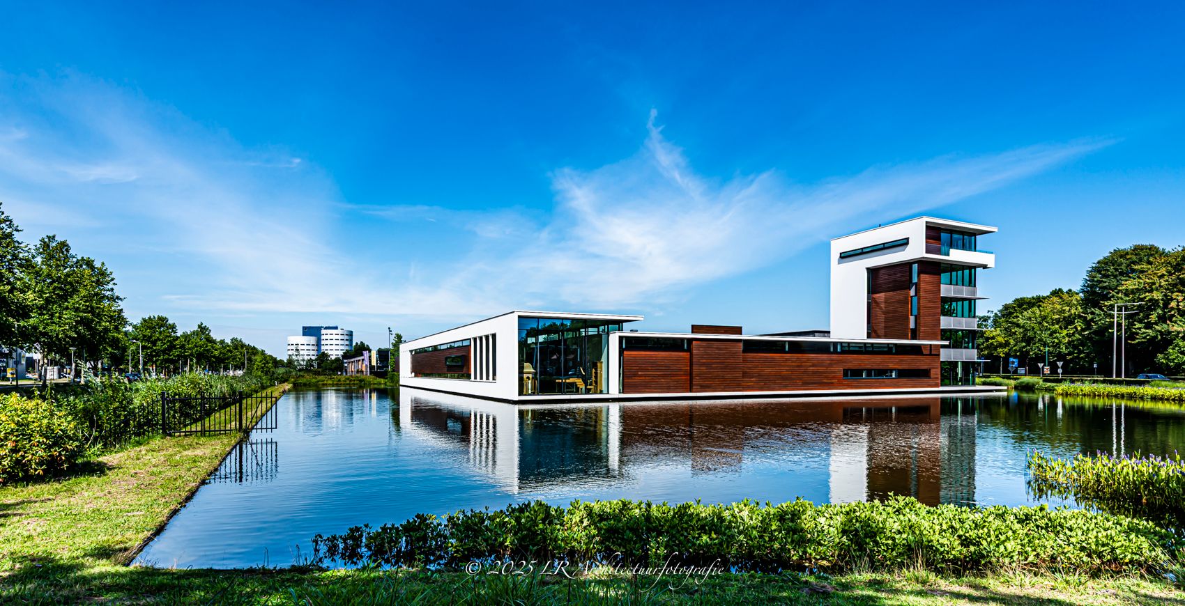 Een modern gebouw dat symmetrisch weerspiegelt in het water eronder, onder een blauwe lucht.