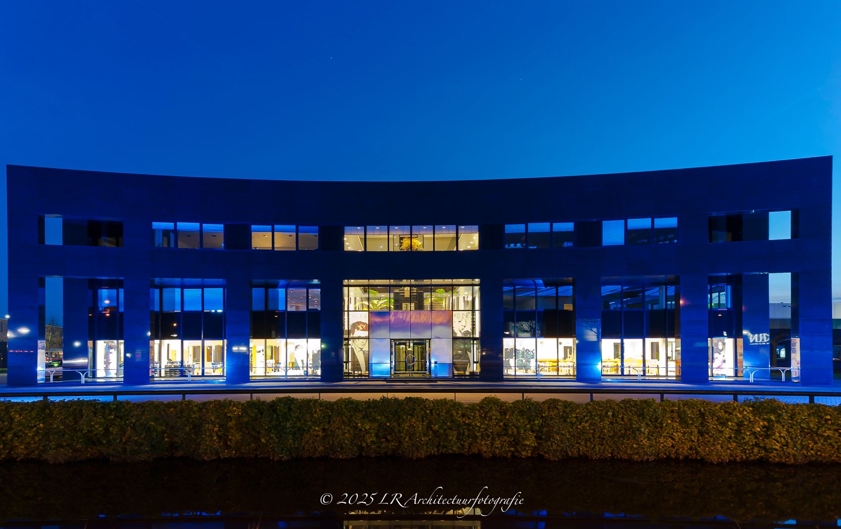 Een gebouw in het blauwe uur met warm verlichte ramen tegen een diepblauwe lucht.