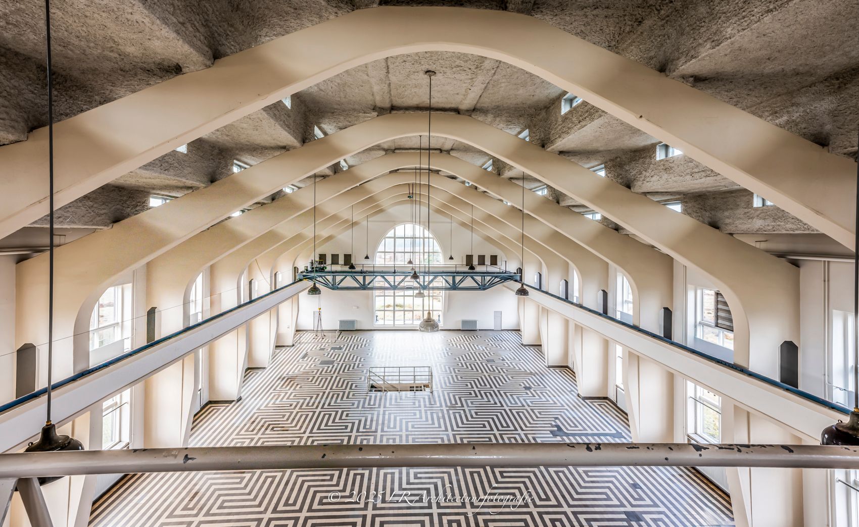 Een gewelfde betonnen hal, warm uitgelicht zodat de ronding van het plafond oplicht.