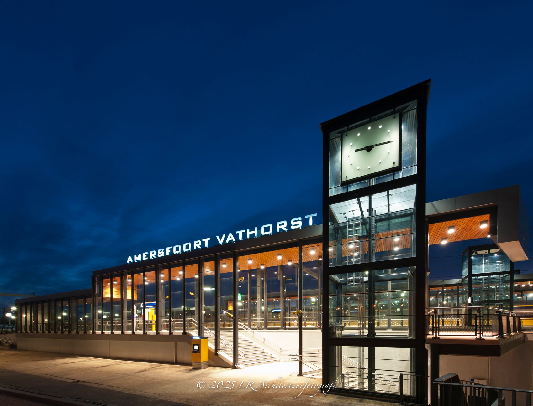 Een glazen gevel die 's avonds van binnenuit oplicht.