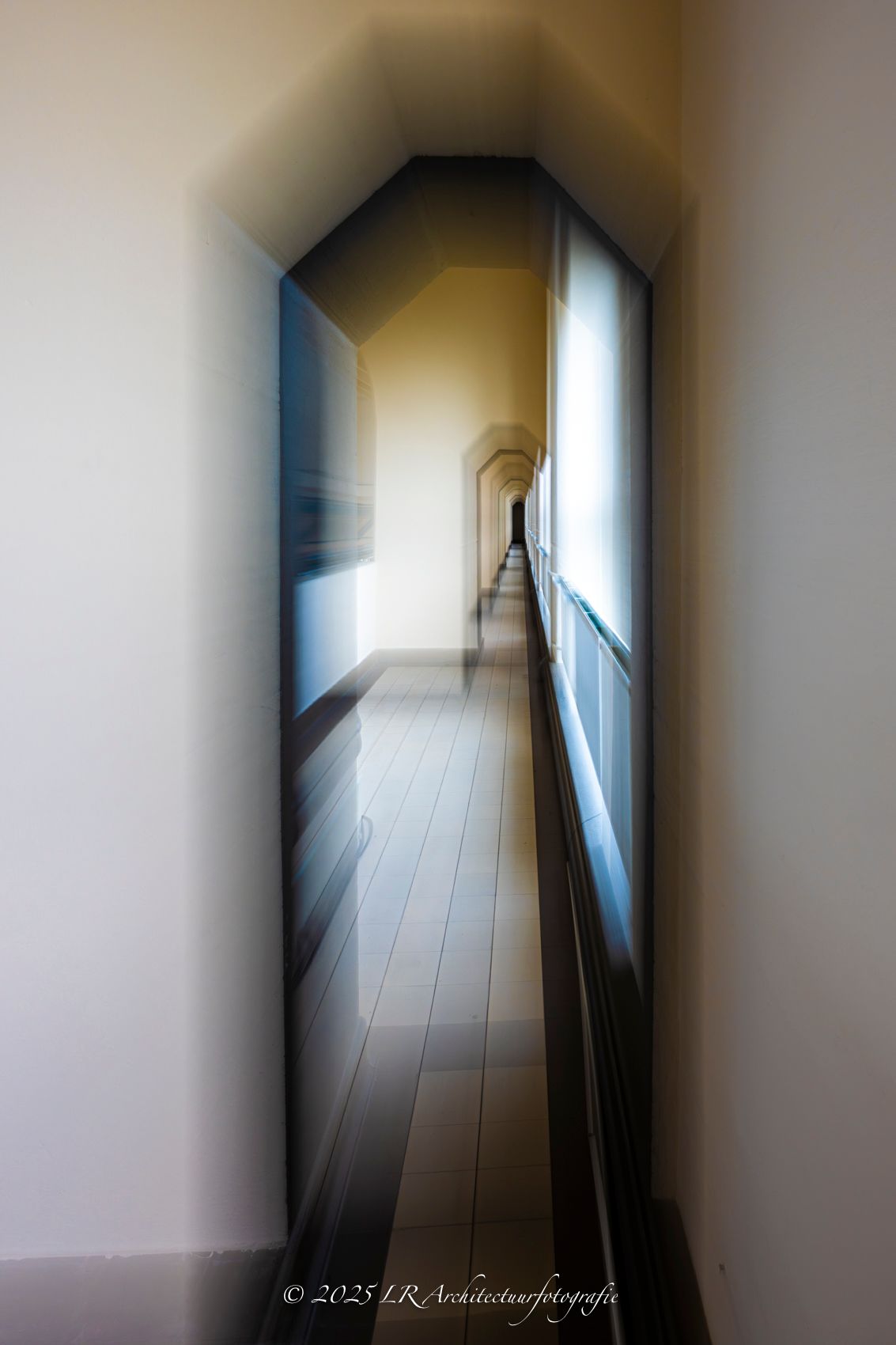 Een verticaal interieurdetail waarin licht en schaduw langs een strakke wand spelen.
