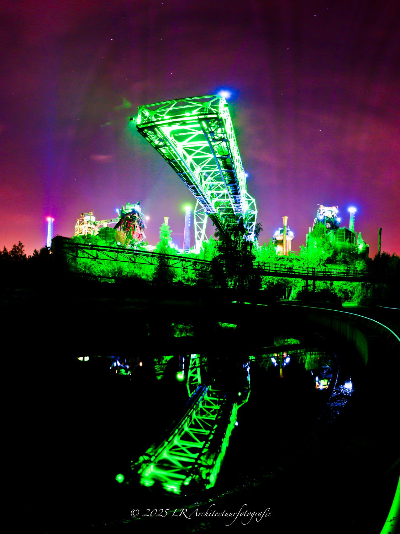 Groene laserstralen van een lichtkunstwerk waaieren uit over een nachtelijke locatie.