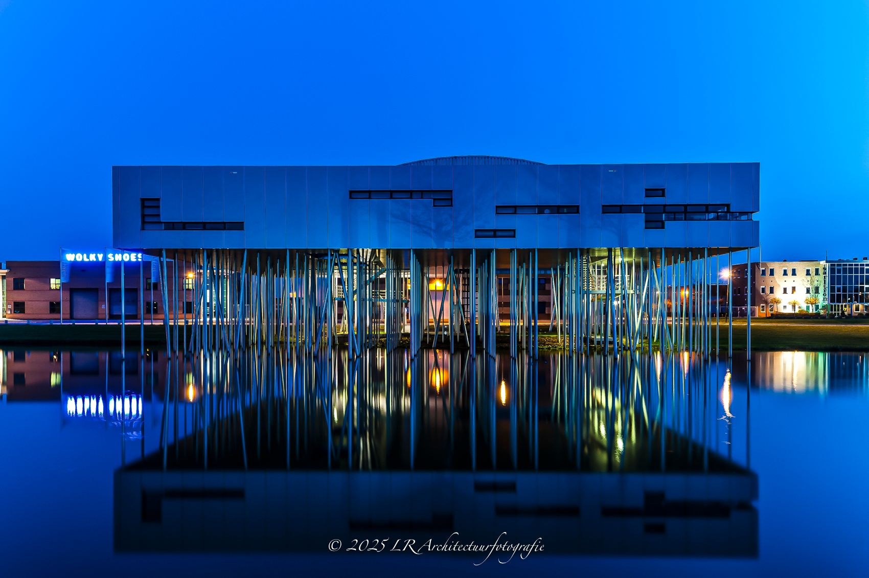 Een strak modern gebouw in de schemering, met warm licht achter de gevel.