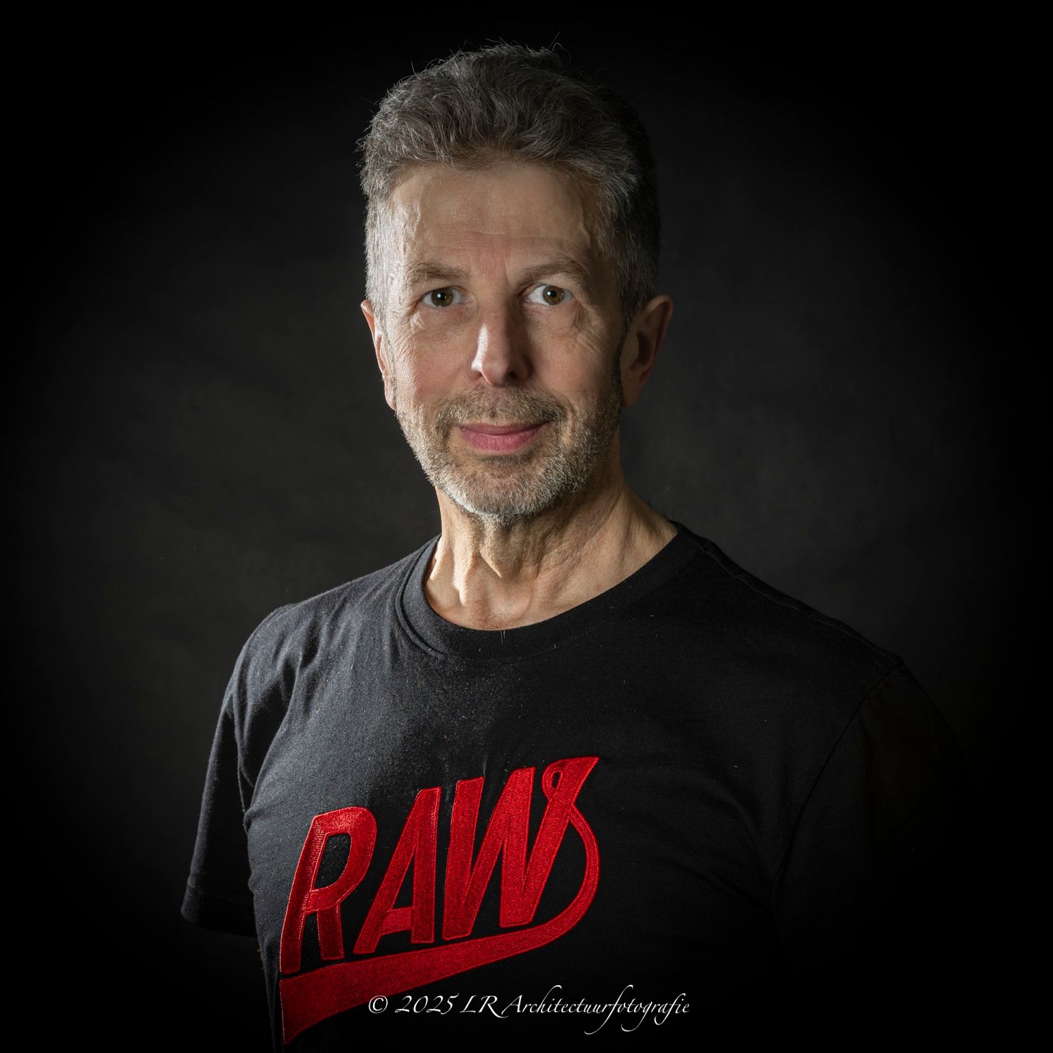 Portret van fotograaf Leo Rieksen, grijzend haar en baard, rustige blik, in een donkere studio.
