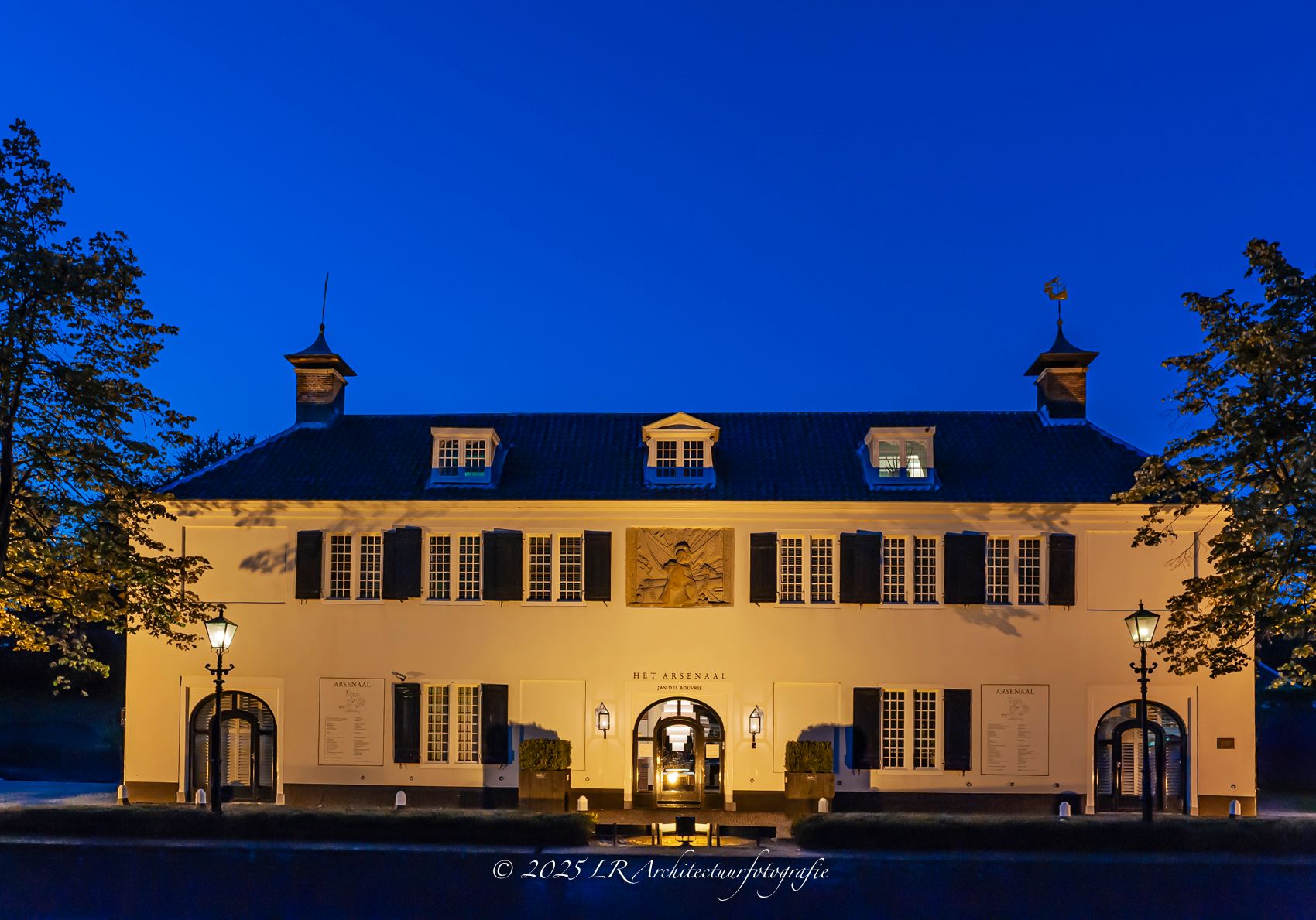 Een symmetrische witte villa met parkaanleg ervoor, in helder daglicht.